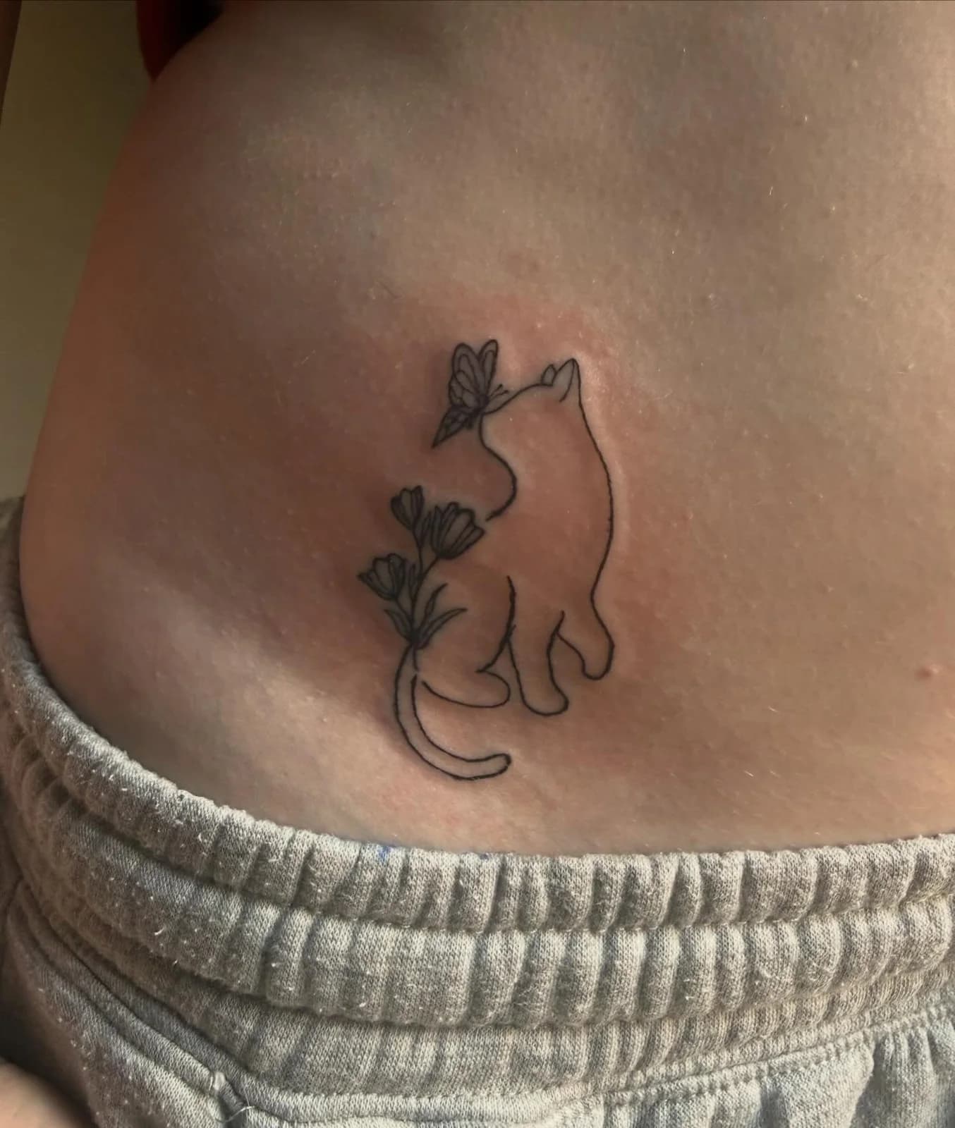 Minimal outline tattoo of a cat holding a flower